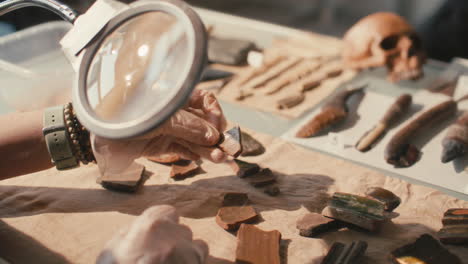 gloved hands of researcher examining artifact fragment with magnifying glass