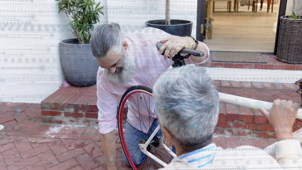 Bearded man spotting loose axle, kneeling, tightening wheel during repair, helper holding frame