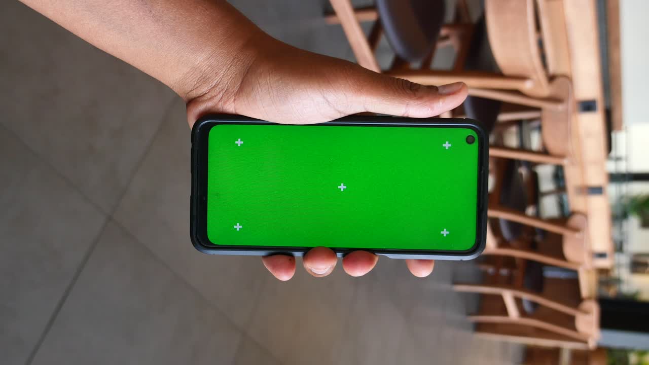 Person holding a smartphone with green screen in a cafe