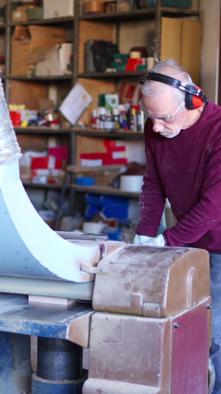 Uomo anziano che leviga il legno con una macchina in un'officina.