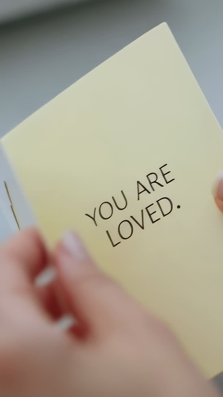 Video verticale: mani che scelgono un biglietto a forma di cuore e che fanno scorrere un inserto chiaro su una scrivania con la scritta TI AMO
