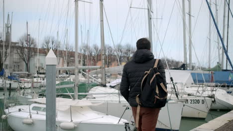 man walking along a harbor pier with sailboats