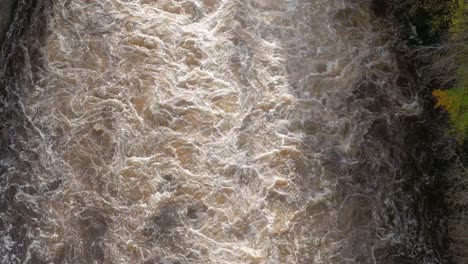 Drone footage flying directly over a raging river as light ctaches the foam and pume