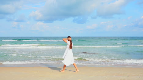 En-Cámara-Lenta,-Una-Mujer-Joven-Vestida-Con-Un-Vestido-Suelto-Camina-Por-La-Playa