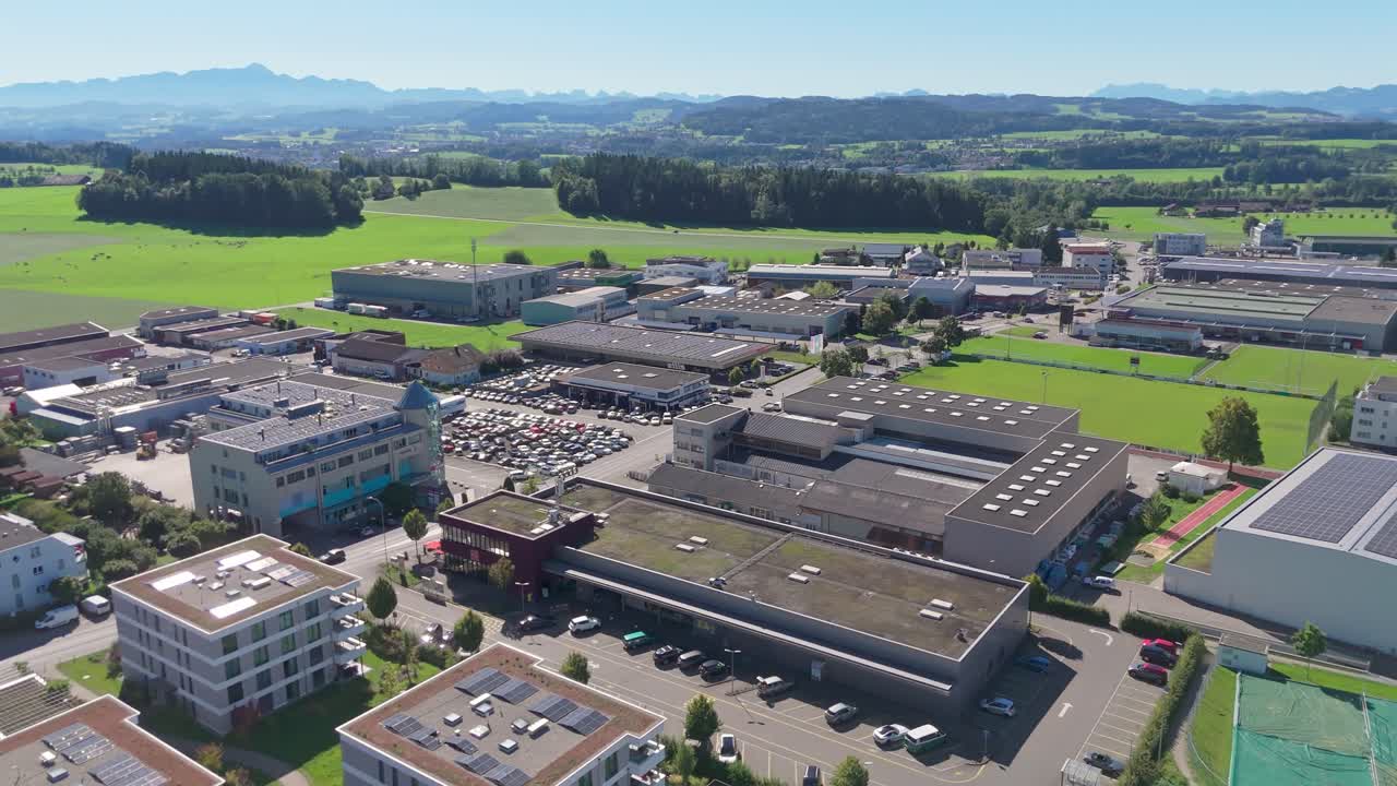 Drone flight over Swiss town with luxury similar apartment buildings in summer. Idyllic landscape with meadow and alps in distance. Peaceful scene. Wide shot