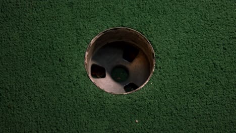 a close up birds eye view of a purple mini golf ball misses the hole on a course