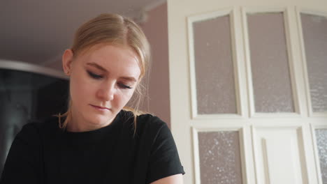 light skin woman wearing black shirt looking down with calm focus in softly lit indoor room, white paneled door with frosted glass in background, showing serene moment of concentration and presence
