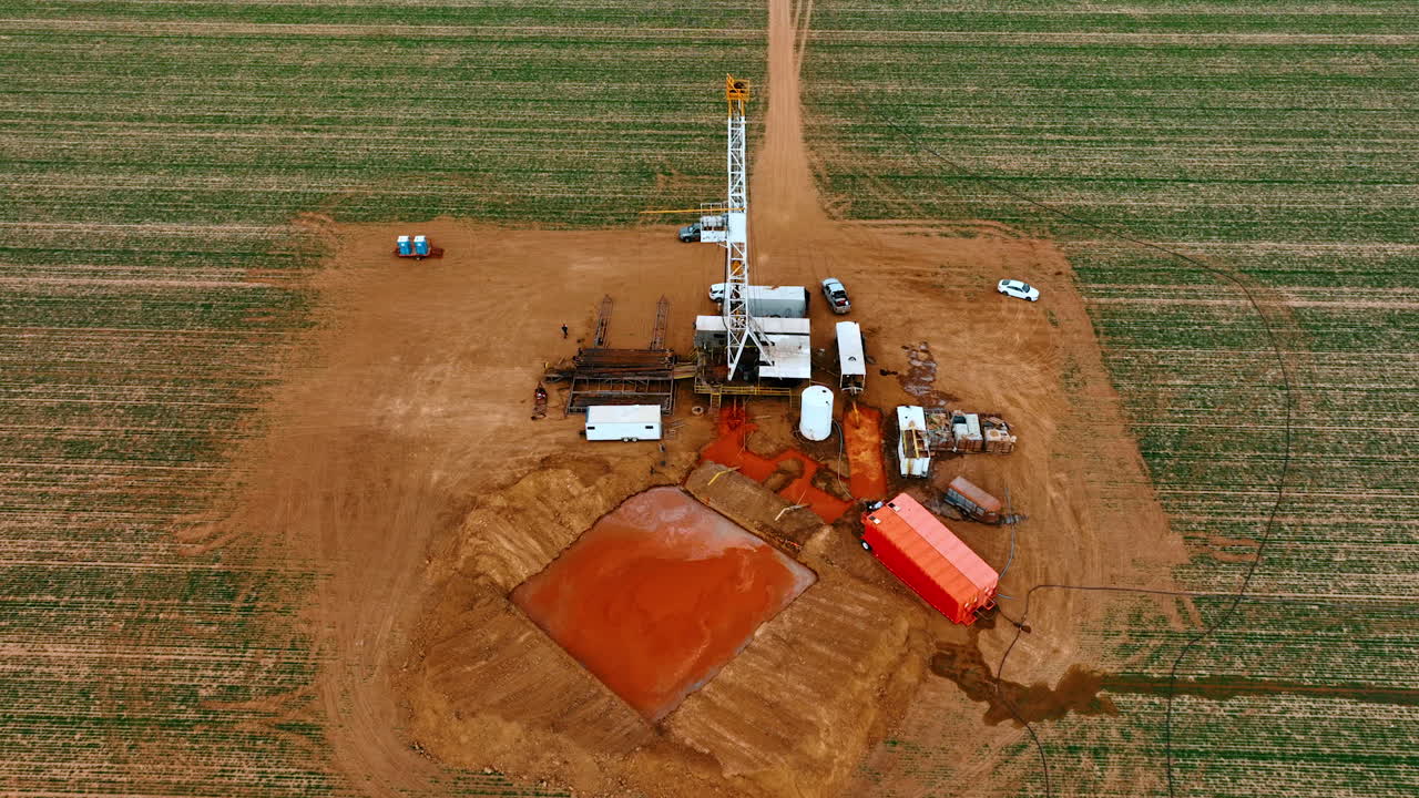 Vast field with the site for natural resources production. Aerial perspective at the location with equipment for drilling and pool filled with orange water.