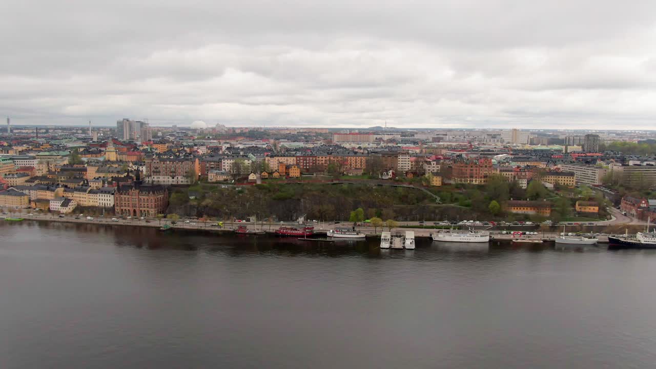 Dolly right aerial over Södermalm, Stockholm, early spring day with very cloudy skies, showcasing urban life and serene waters
