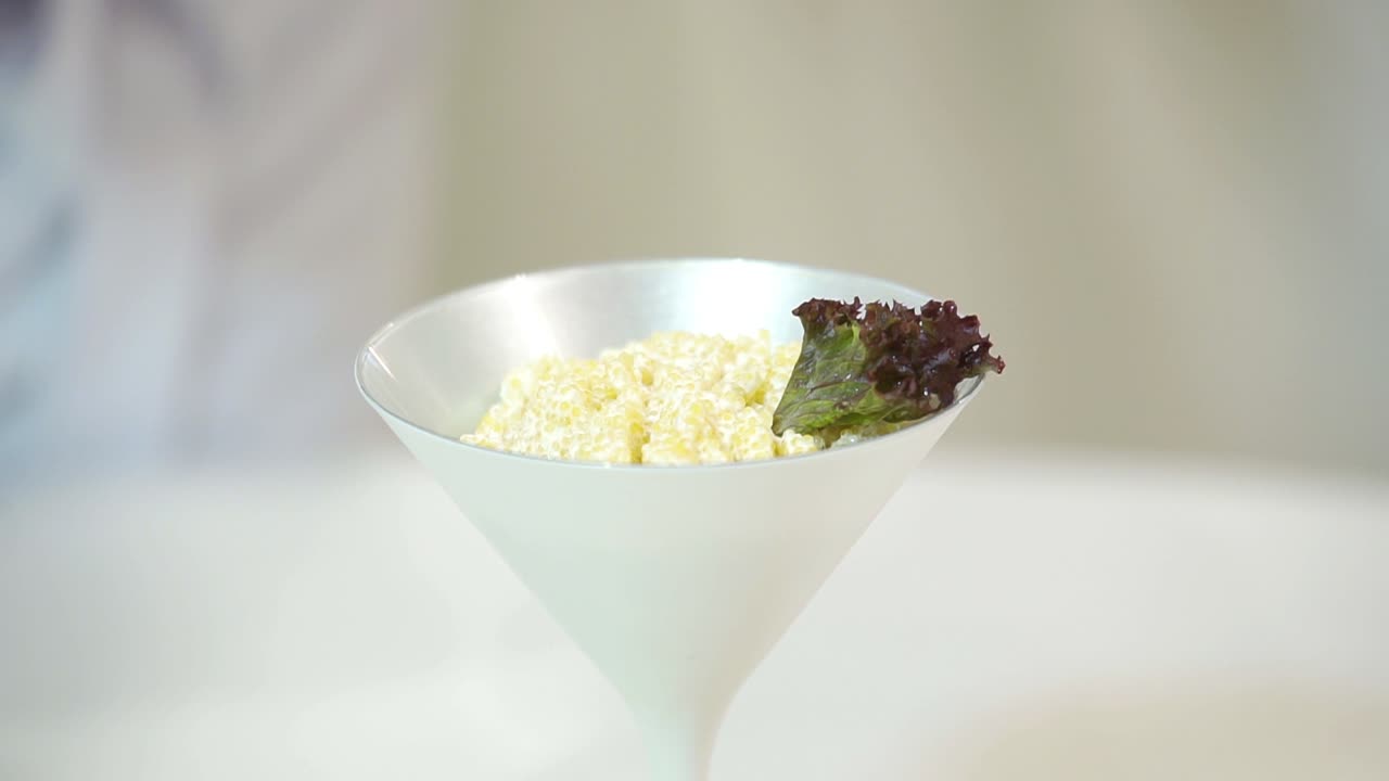 A chef serves the dish in a white ceramic bowl using cherry tomato pieces and salad leaves on the white background. Close-up.