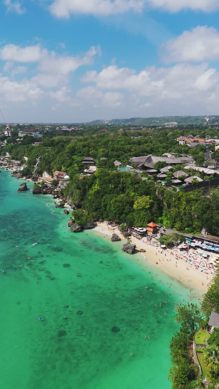 Vertical aerial view, Padang Padang Beach in Uluwatu, Bali, Indonesia. Clear turquoise water, sandy shoreline and tropical greenery showcase a famous travel destination
