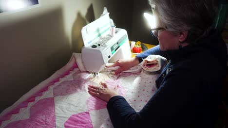 senior woman using a sewing machine to stitch a pattern on a handmade quilt