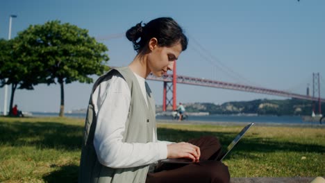 woman working on laptop in a park, near the bridge of april 25 in lisbon