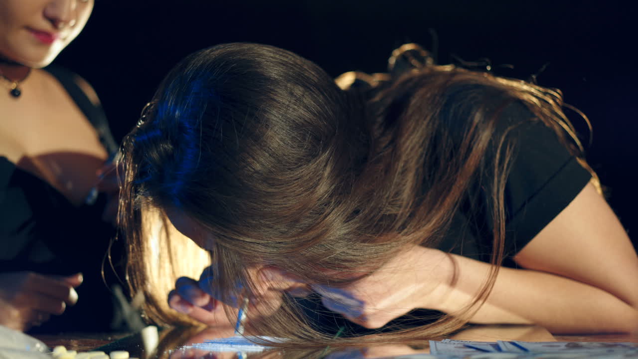 Two brunette girls snort cocaine on a mirror with a roll of banknotes. Drug Abuse
