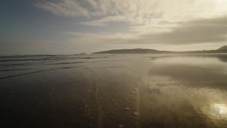 Kleine-Wellen-An-Einem-Wunderschönen-Strand-Bei-Sonnenuntergang,-Wobei-Sich-Das-Licht-Im-Sand-Spiegelt