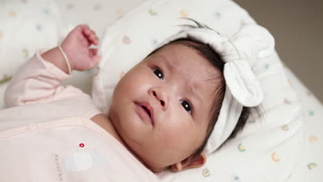 winching her face as she hiccups, the newborn baby girl is looking up as she is lying on her pillow inside her crib