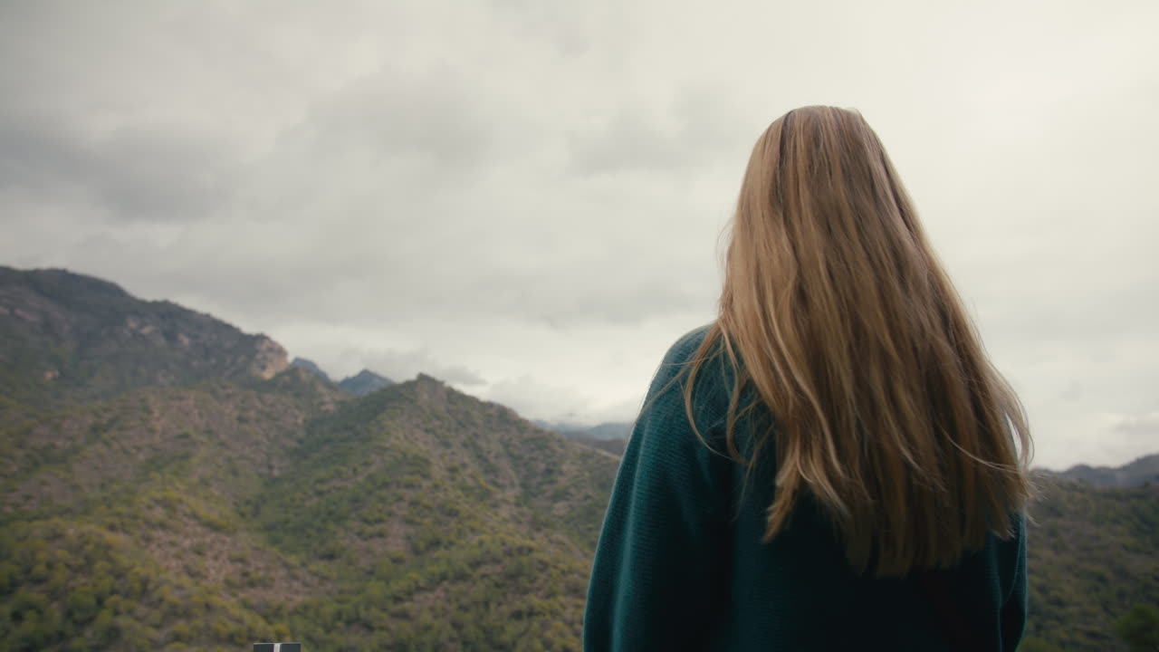 Uma mulher com cabelo loiro comprido observa montanhas verdes em um dia nublado no sul da Espanha.