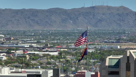 bandera estadounidense y bandera del estado de arizona ondeando frente a los suburbios de la ciudad en expansión y el gran paisaje montañoso