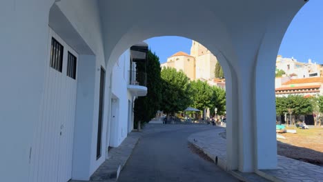 Reveal-shot-of-the-church-of-Cadaques-on-the-Costa-Brava-of-Girona,-arches-of-the-tunnel-bridge-in-front-of-the-Mediterranean-Sea