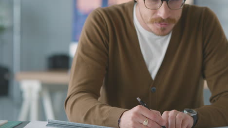 Nahaufnahme-Eines-Männlichen-Architekten-Im-Büro,-Der-Am-Schreibtisch-Mit-Einem-Gebäudemodell-Arbeitet-Und-Notizen-Zum-Plan-Macht