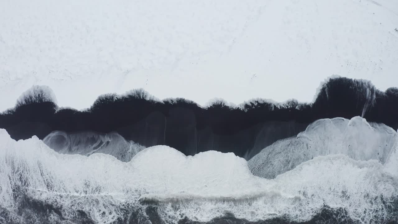 아이슬란드 검은 해변의 아름다운 드론 샷은 바다의 높은 파도와 흐린 날씨를 보여주고 눈은 검은 모래의 일부를 덮고 있습니다.