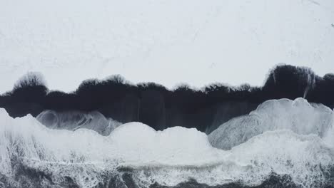 una hermosa toma de drones de la playa negra en islandia muestra las altas olas del mar y el clima nublado mientras la nieve cubre parte de la arena negra