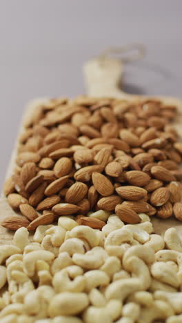 video vertical de nueces de almendra y caju apiladas en una tabla de cortar de madera con fondo de lila