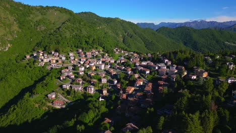 wide aerial view of a mountain village with red rooftops, surrounded by forested hills under a vibrant blue sky. shot at selvino, italy (selvino, italia)