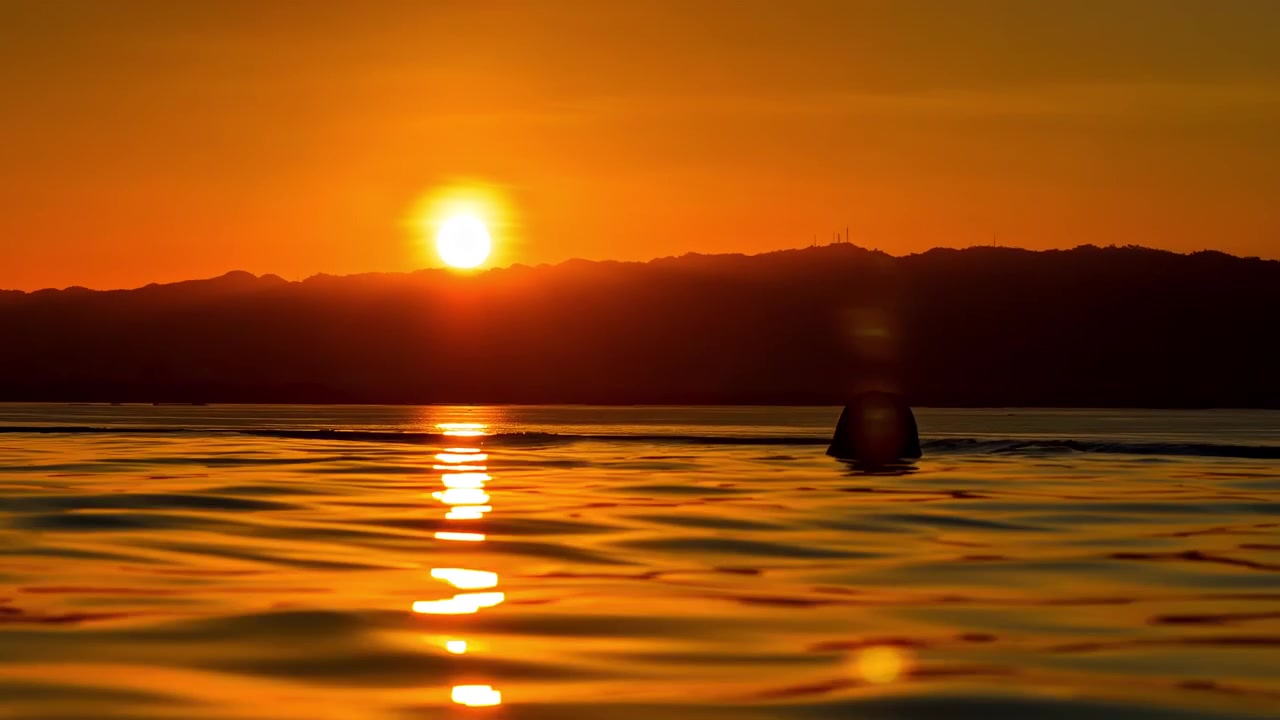 Naisen siluetti ui vastavirta-altaassa upean auringonlaskun aikaan, rauhallinen matkahetki