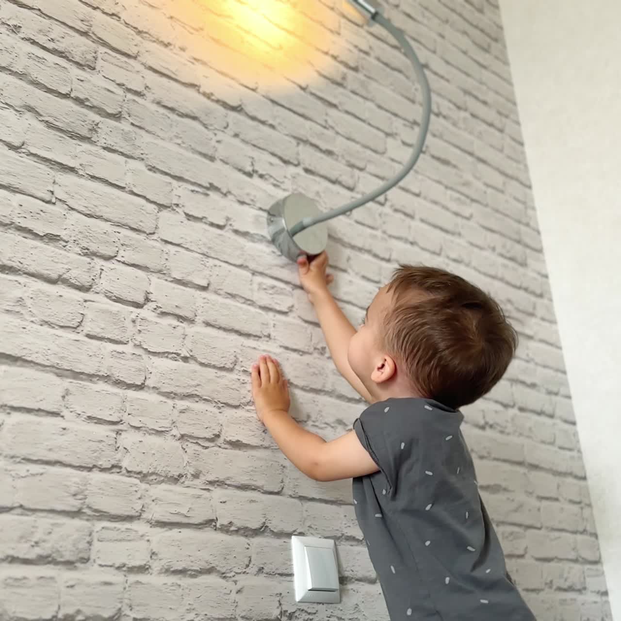 Baby boy playing with the lamp on the wall. Kid reaches the light switch and is happy to turn on the light. Low angle view