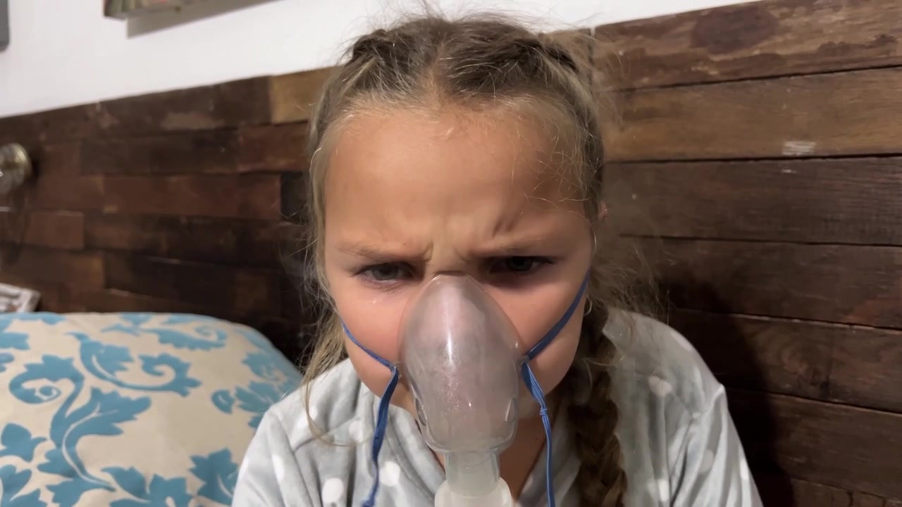 Mladá dívka s copánky má na sobě nebulizační masku rozprašující Ventolin pro léčbu astmatu.