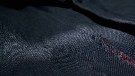 a closeup image of fabric detailing a noticeable red stain on dark material, emphasizing the wear of the textile