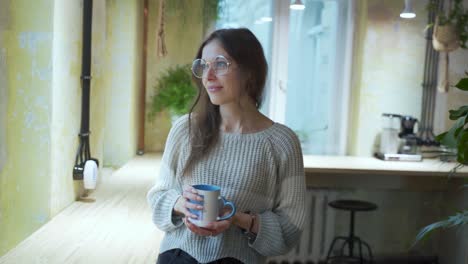 young european female student is enjoying her coffee or tea at the coffeehouse with natural background