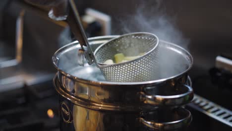 steamy cooked pasta in a steel scoop colander over stainless pot