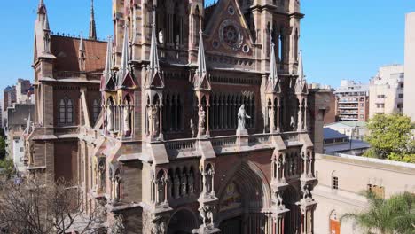 Elevation-aerial-view-of-gothic-architectural-style,-church-of-capuchinos,-sacred-heart-of-Jesus,-reveals-dense-population-of-downtown-cityscape-against-clear-blue-sky