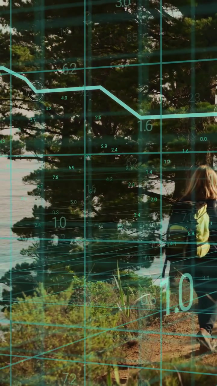 Vertical video: Female hiker walking trail by water, tech HUD appearing over hiker updating graphs