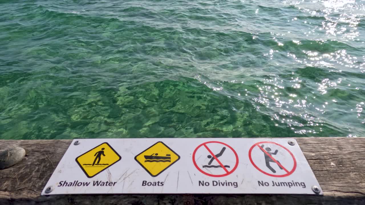 Warning signs on a pier highlight safety measures against diving and boating in shallow waters