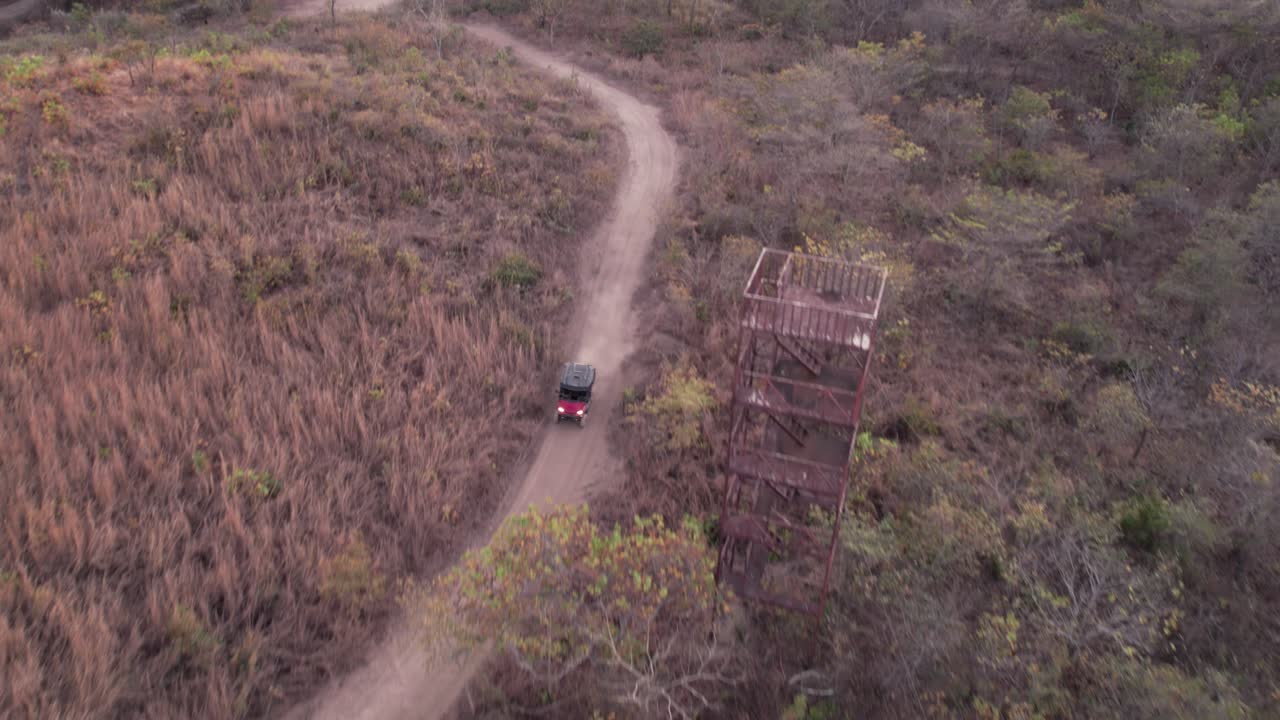 Drone view of an off-road vehicle driving along a winding dirt trail surrounded by forested hills during sunset in Costa Rica
