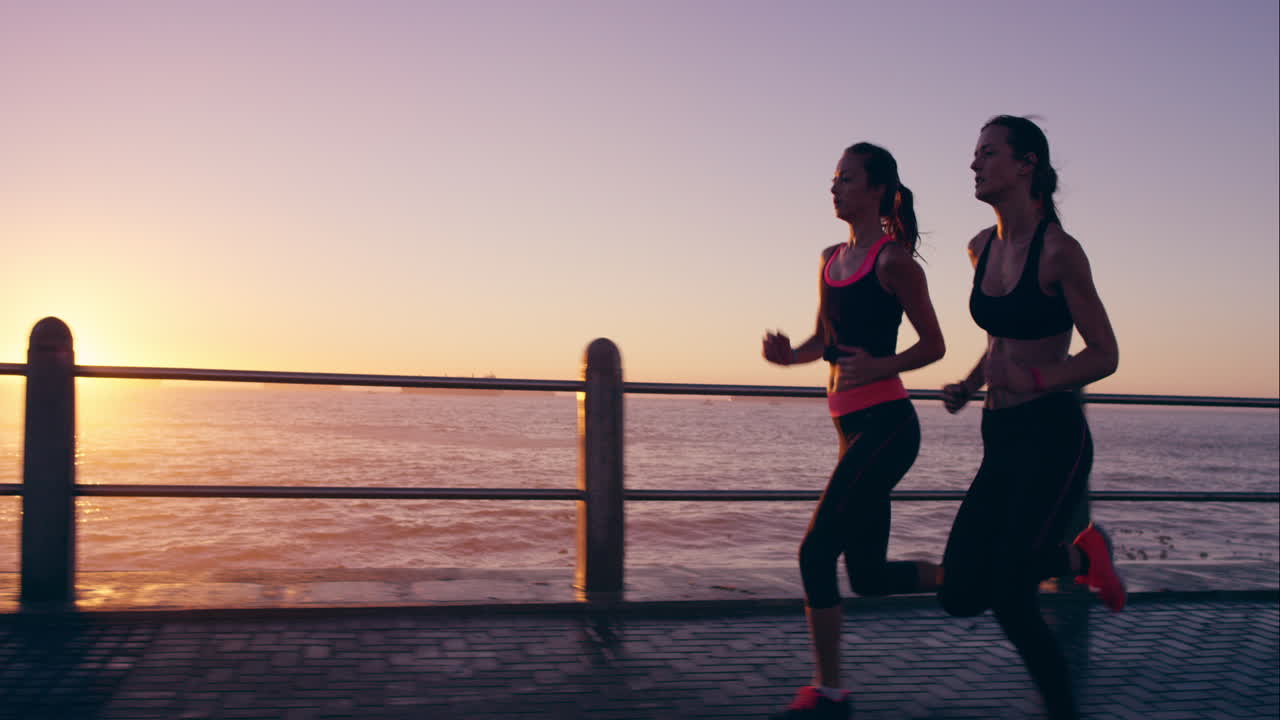 dos mujeres atléticas corriendo al aire libre en cámara lenta en el paseo marítimo al atardecer cerca del océano disfrutando de la carrera nocturna