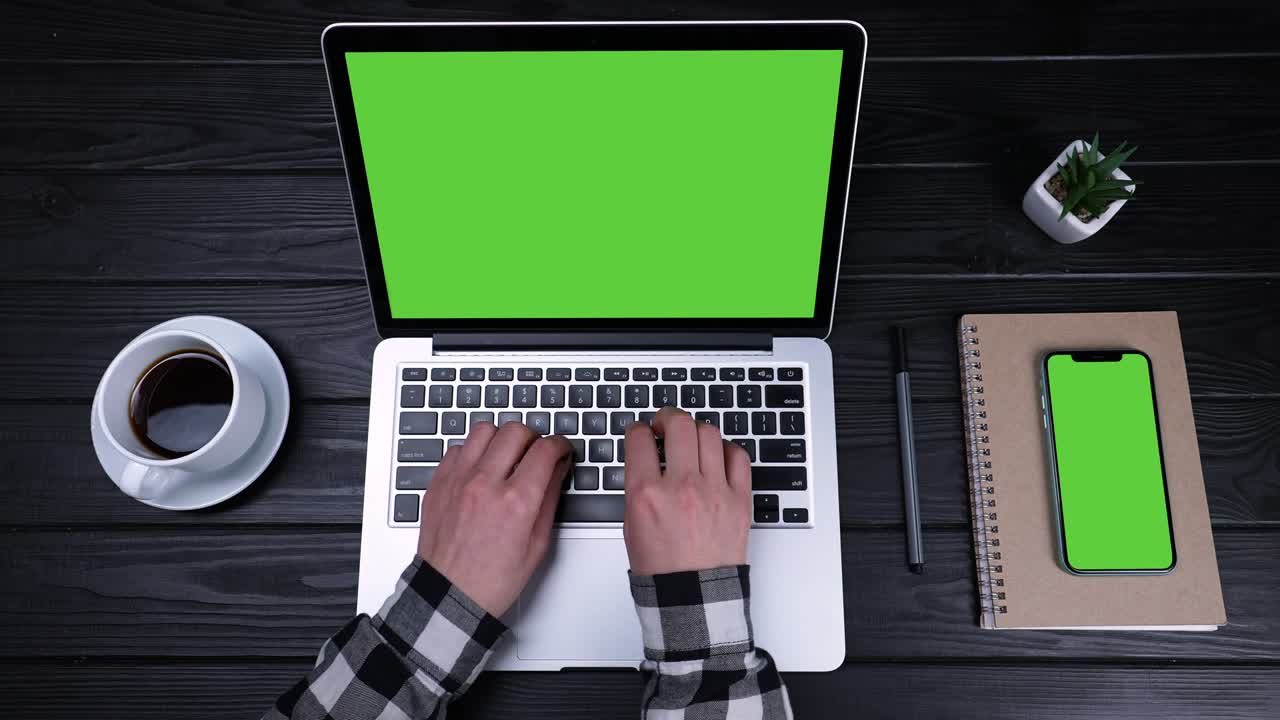 Female hands are typing on a laptop keyboard with a green screen and a chrome key. On the table next to the laptop is a smartphone with a green screen and a chrome key. Slow motion. Close up
