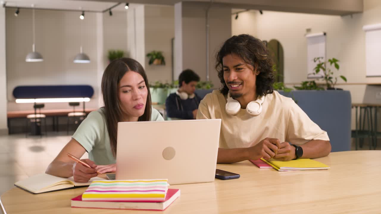 African American man approaching Hispanic woman at table, leaning in, discussing laptop project