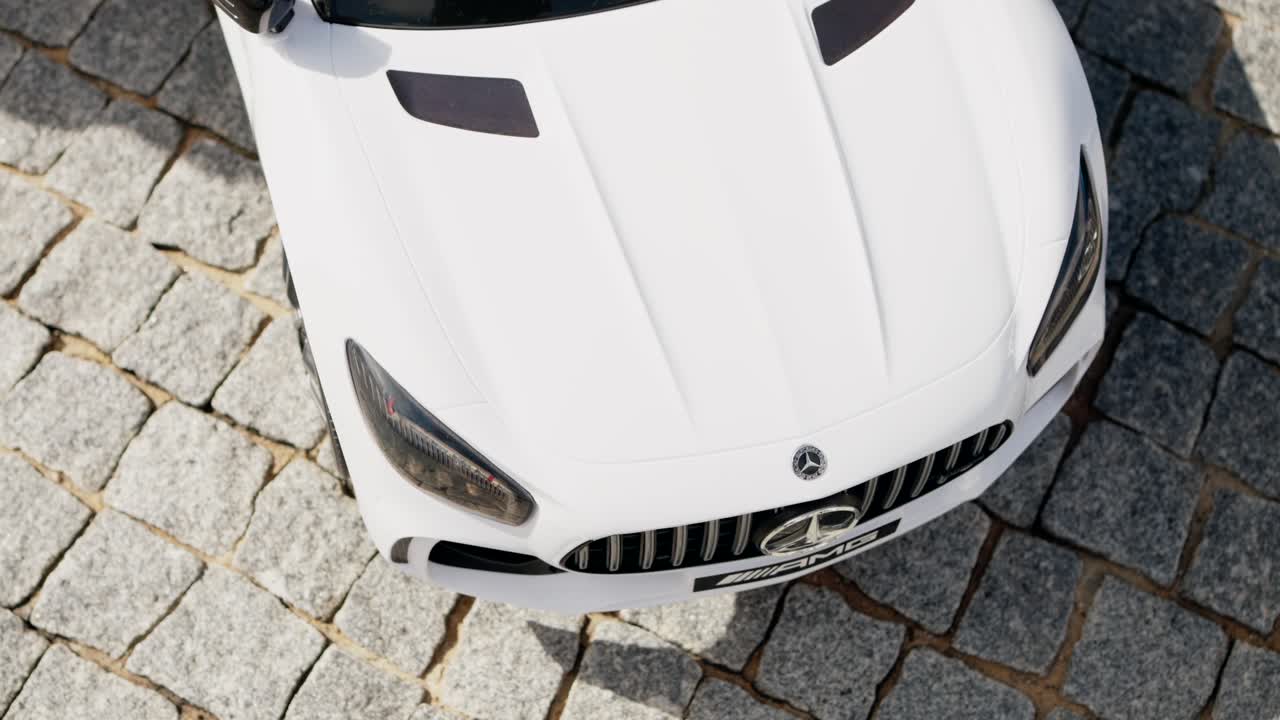 White miniature Mercedes toy car on cobblestone pavement, viewed from above