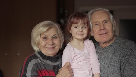 Grandfather-and-grandmother-kissing-on-cheeks-their-kid-granddaughter-at-home