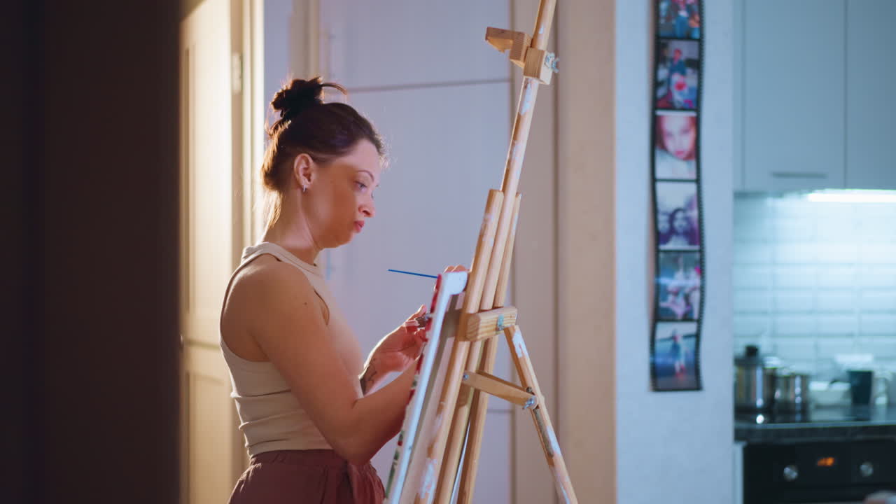 Young White Woman Painting On Easel In Cozy Kitchen Studio, Independent Illustrator Sketching Intimate Floral Canvas Under Warm Lamp Light, Focused Expression, Palette And Brushes, Textured