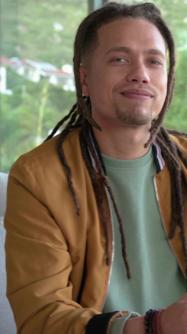 Vertical video: Glancing right, man in brown jacket sipping green mug at home, responding to voice