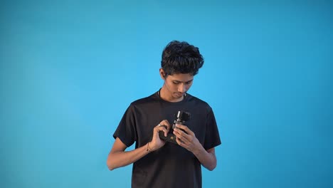 Boy-photographer-is-taking-some-still-with-his-DSLR-camera-and-checking-the-new-camera-body-in-black-t-shirt-and-blue-colored-indoor-studio-background