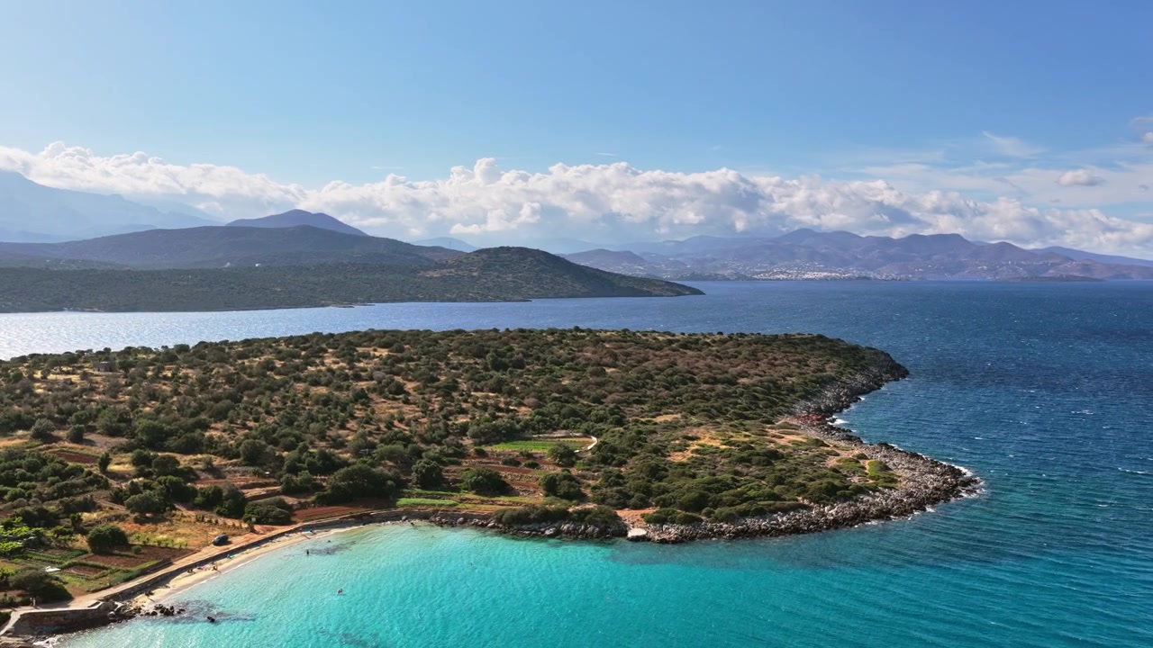 Letecký pohled dronem na zelený zalesněný poloostrov a malou tyrkysovou zátoku v širokém zálivu obklopeném horami, pláž Voulisma, Řecko