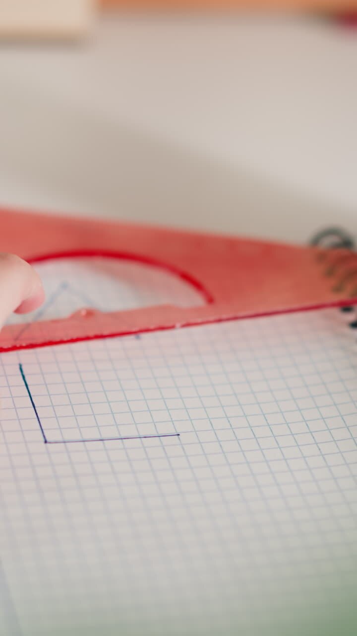 Little student draws triangular shape with ruler and pen on copybook page at desk closeup. Schoolgirl studies figures doing homework at home