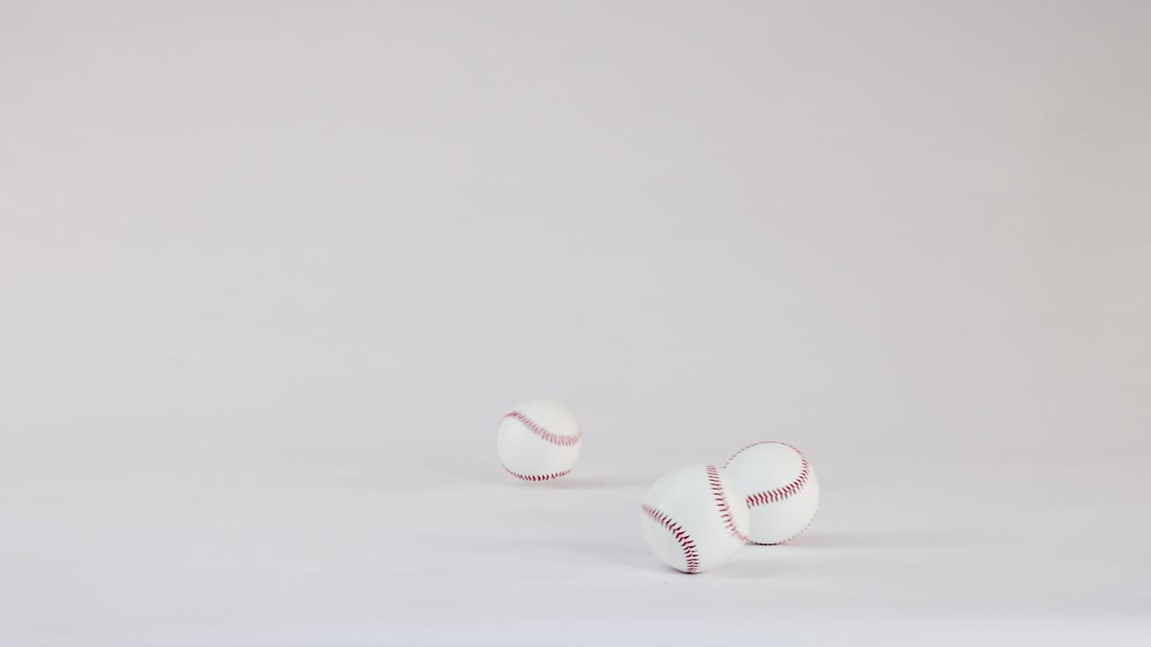 Tre palle da baseball bianche con cuciture rosse rimbalzano e rotolano su un pavimento di uno studio bianco brillante