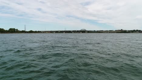 A-drone-flies-over-Lake-Erie,-capturing-the-Fort-Erie-Peace-Bridge-in-the-background